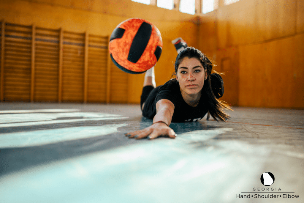 A volleyball player diving for a ball with her extended hand flat against the floor where wrist and finger impact occurs, in Atlanta.